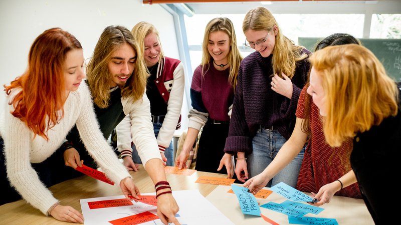 Studenten HVHL staan om tafel en brainstormen met papier en post-its