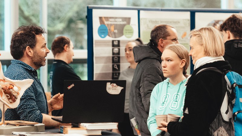Sfeerimpressie van HVHL open dag met student en ouders in gesprek met docent