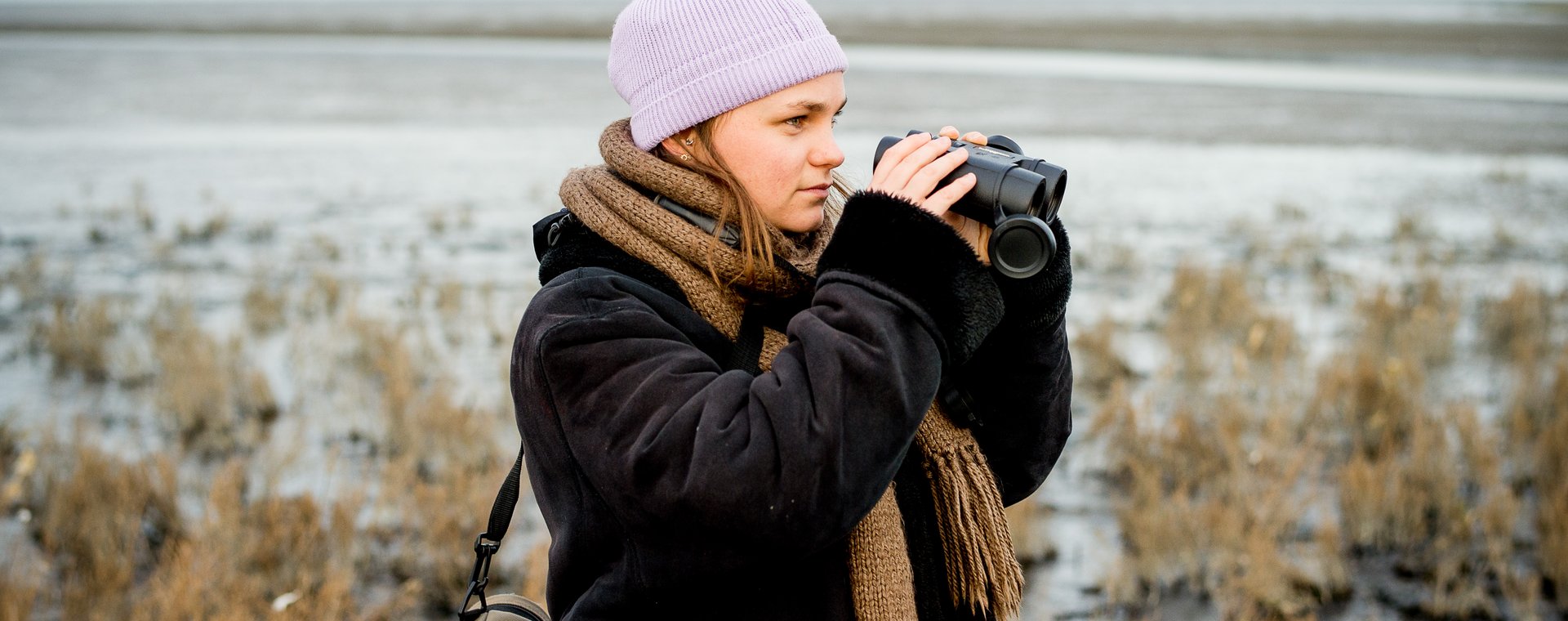 Studente hbo-opleiding Kust- en Zeemanagement kijkt door een verrekijker naar het wad.