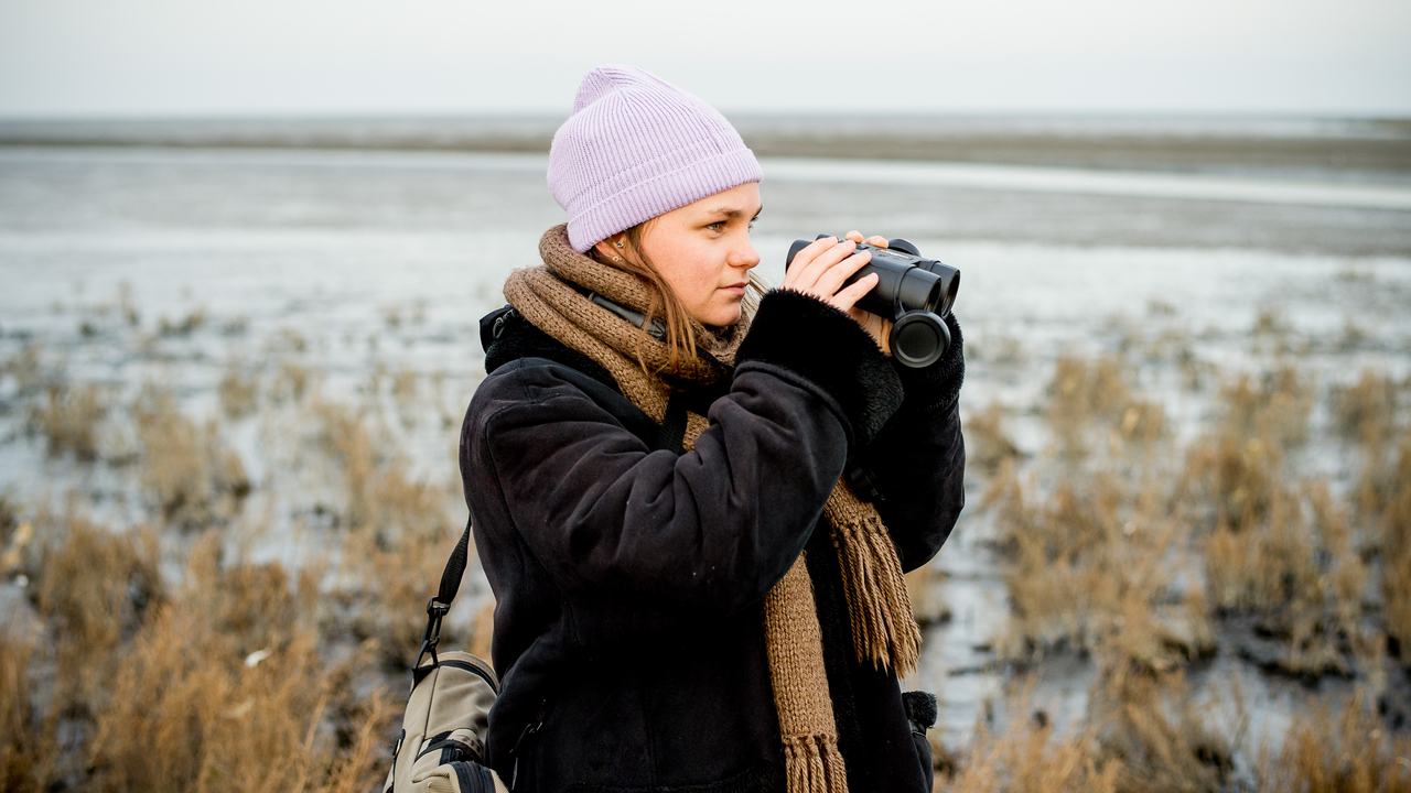 Studente hbo-opleiding Kust- en Zeemanagement kijkt door een verrekijker naar het wad.