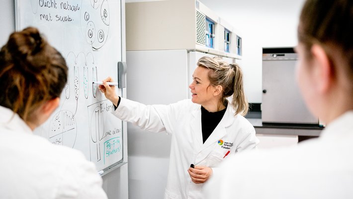 Twee studenten Biotechnologie krijgen in lab uitleg op whiteboard van docent