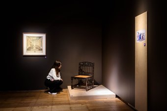 Bezoeker bestudeert kerkstoel (1850-1930). Collectie Stichting Nationaal Museum van Wereldculturen. Foto Mike Bink.